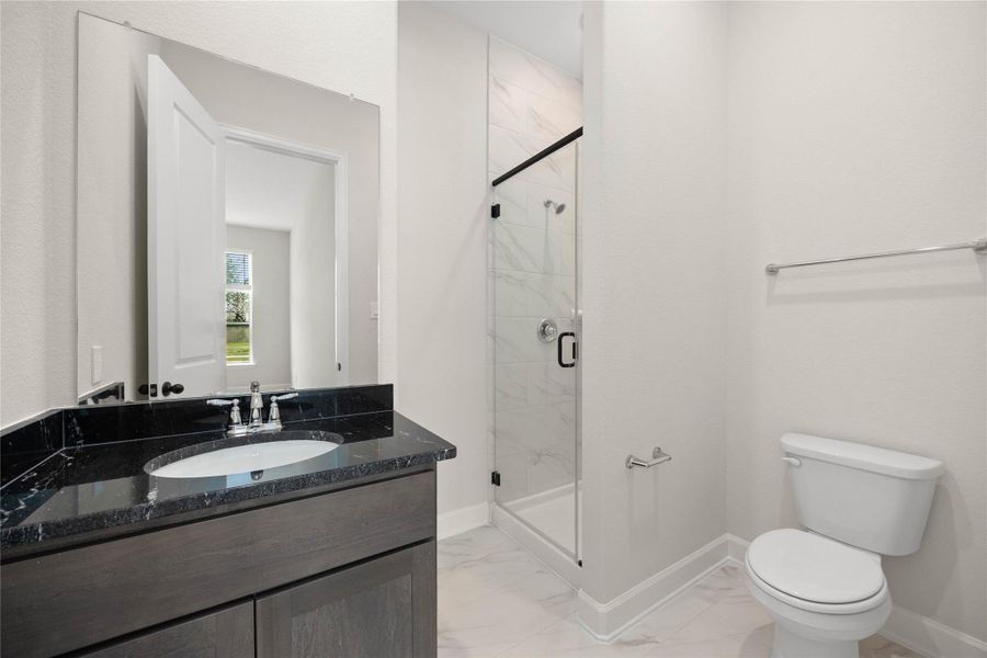 Modern ensuite bathroom featuring premium finishes and a sleek, contemporary design. This private bath boasts a dark wood vanity topped with elegant black granite countertops, a large vanity mirror, and matching chrome hardware. The standout walk-in shower showcases floor-to-ceiling marble-patterned tiling, a seamless glass enclosure, and modern black trim accents, creating a spa-like retreat for guests or family. Modern ensuite bathroom featuring premium finishes and a sleek, contemporary design. This private bath boasts a dark wood vanity topped with elegant black granite countertops, a large vanity mirror, and matching chrome hardware. The standout walk-in shower showcases floor-to-ceiling marble-patterned tiling, a seamless glass enclosure, and modern black trim accents, creating a spa-like retreat for guests or family.