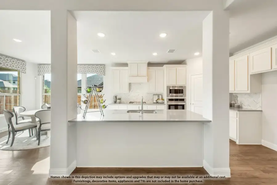 Open kitchen with white cabinets, large island, herringbone tile backsplash, and stainless steel appliances, adjacent to dining area.