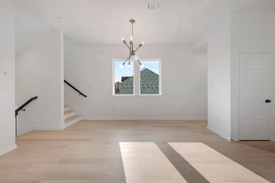 Open-concept room featuring light wood-finish flooring, white walls, and a contemporary chandelier