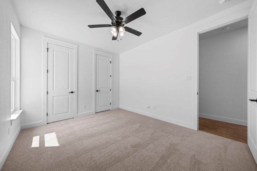 Unfurnished bedroom with light carpet, ceiling fan, and two closets