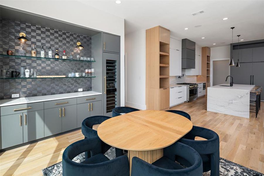 Stylish built-in bar featuring custom cabinetry, a striking textured tile backsplash, floating glass shelves, and elegant accent lighting. Complete with a built-in wine refrigerator and generous serving space, this area is perfectly designed for entertaining and elevating the dining experience.