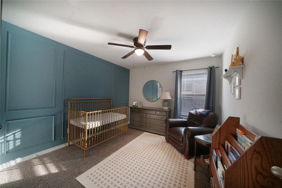 Bedroom with a nursery area, carpet floors, ceiling fan, and a decorative wall