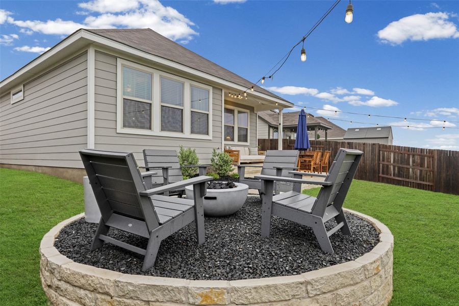 Manicured lawn with a stone-clad raised fire pit area featuring dark gravel and string lighting