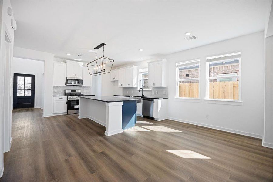 This photo showcases a modern kitchen with sleek white cabinetry, a large island with dark quartz countertops, stainless steel appliances, and ample natural light from three windows. The open layout features wood-style flooring and a stylish light fixture, creating a bright and inviting space. This photo showcases a modern kitchen with sleek white cabinetry, a large island with dark quartz countertops, stainless steel appliances, and ample natural light from three windows. The open layout features wood-style flooring and a stylish light fixture, creating a bright and inviting space.