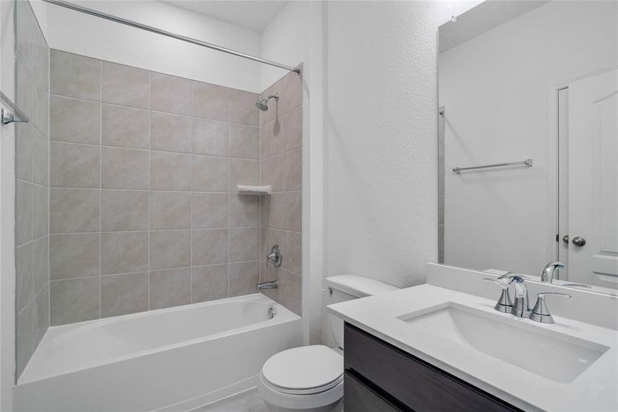 Secondary bath features tile flooring, bath/shower combo with tile surround, stained wood cabinets, beautiful light countertops, mirror, sleek fixtures and modern finishes.