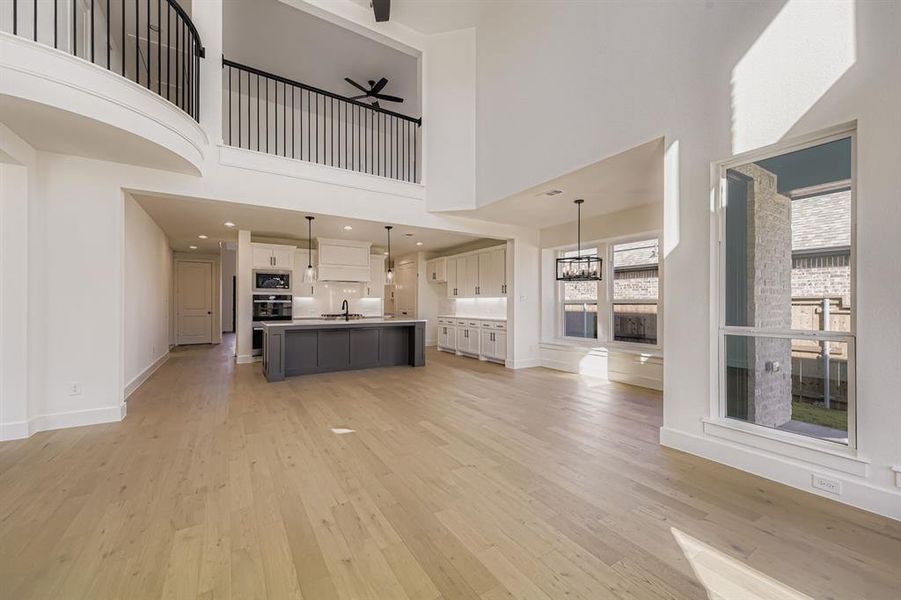 Unfurnished living room featuring light wood-style flooring, a high ceiling, and ceiling fan