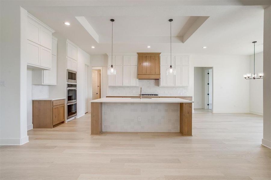 Kitchen with a large island, a raised ceiling, white cabinetry, and pendant lighting