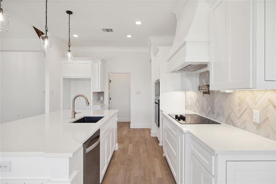 Kitchen with white cabinetry, custom range hood, black electric stovetop, decorative backsplash, and sink