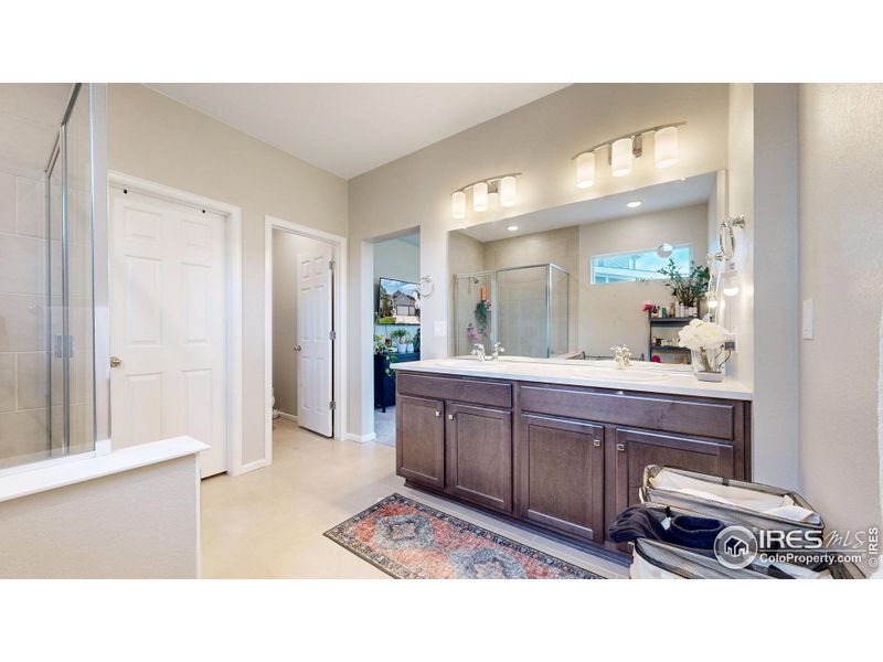 Primary bathroom featuring quartz countertops, dual vanities, a walk-in shower and a large walk-in closet.