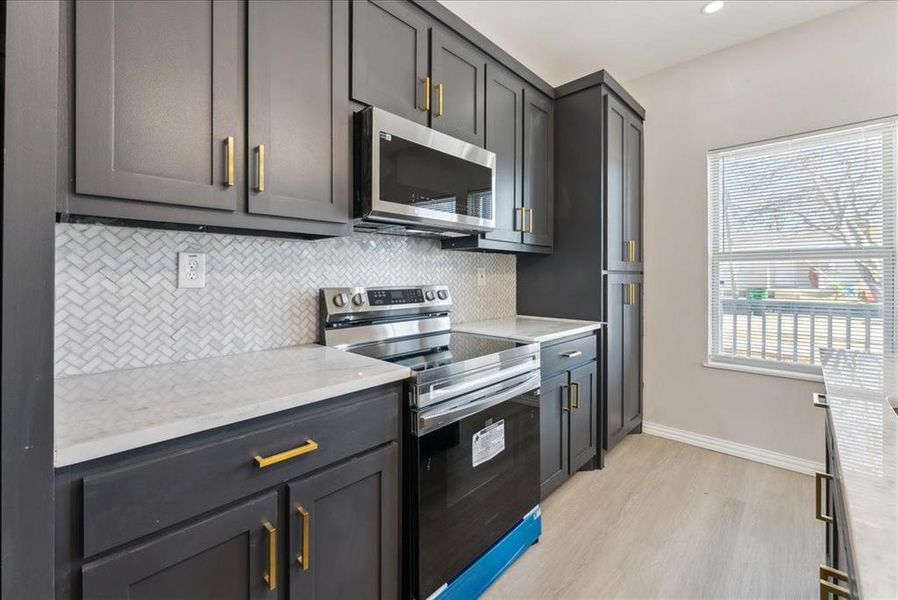 Kitchen featuring light wood finished floors, baseboards, stainless steel appliances, backsplash, and recessed lighting