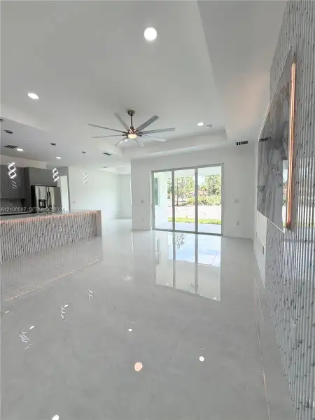 Open-concept area featuring polished stone-finish flooring, recessed lighting, a coffered ceiling with a modern multi-blade ceiling fan, and a kitchen island with stone-finish cladding