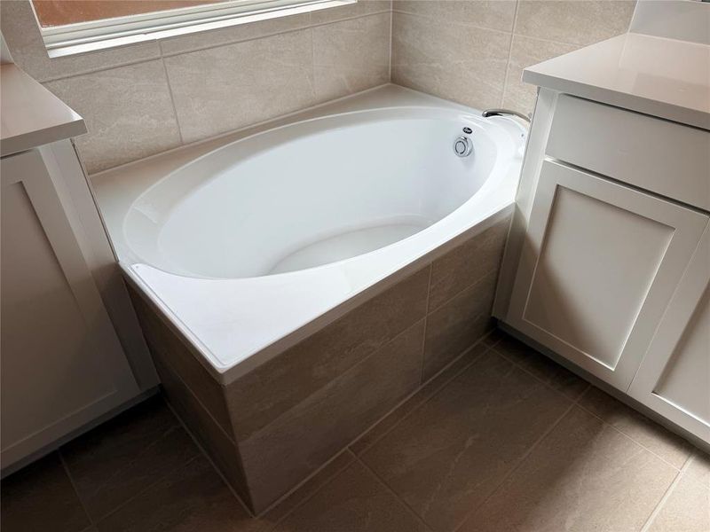 Built-in soaking tub with chrome fixtures, surrounded by light-toned tilework