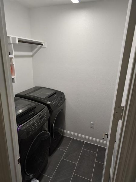 Clothes washing area with dark tile patterned flooring and washing machine and clothes dryer