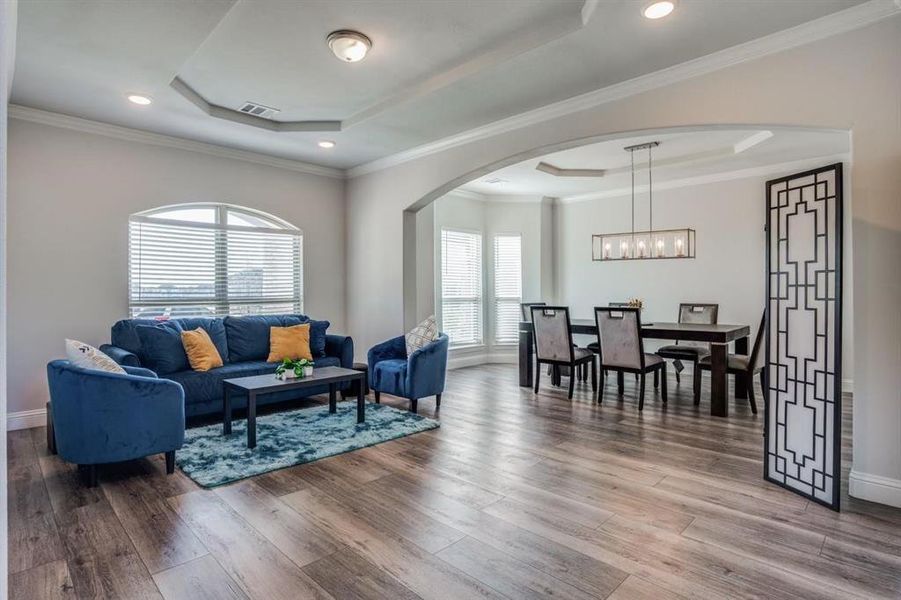 Living room featuring crown molding, wood-type flooring, a chandelier, and a raised ceiling