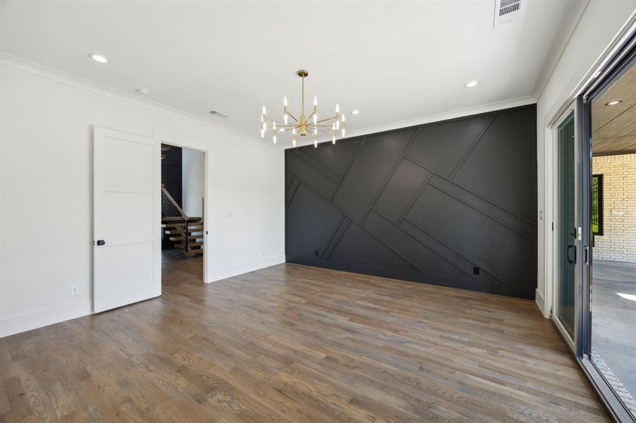 Primary bedroom featuring a chandelier, a decorative wall, visible vents, and ornamental molding Primary bedroom featuring a chandelier, a decorative wall, visible vents, and ornamental molding