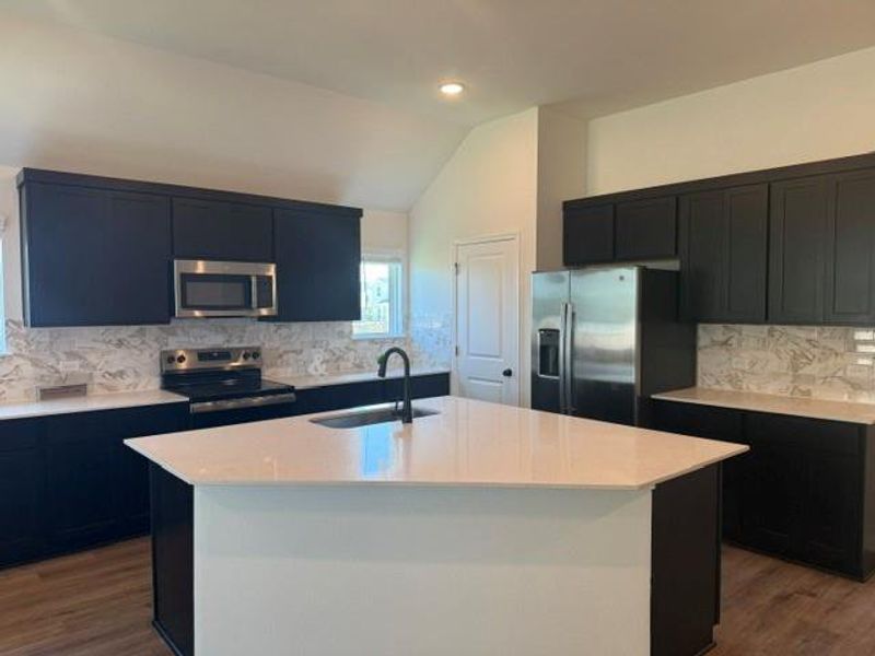 Modern kitchen featuring a central island with a sink, quartz countertops, and matte black cabinetry