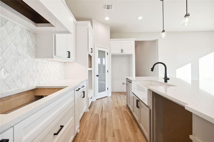 Kitchen with pendant lighting, white cabinets, sink, decorative backsplash, and light wood-type flooring