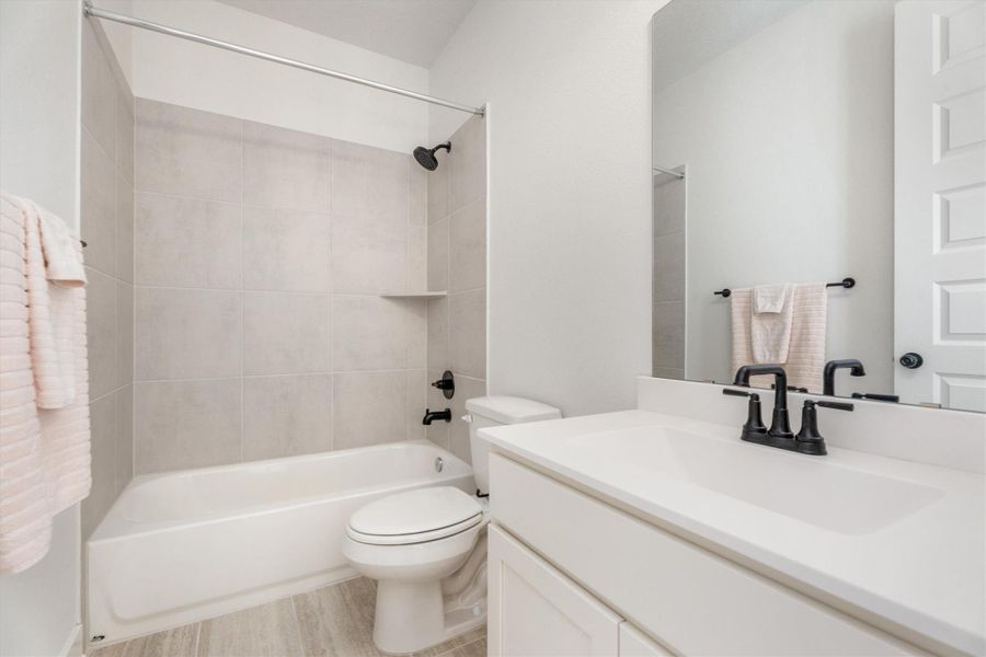 This bathroom features a clean, modern design with a white vanity, sleek black fixtures, and a large mirror. The bathtub is surrounded by light gray tiles, creating a bright and inviting space.