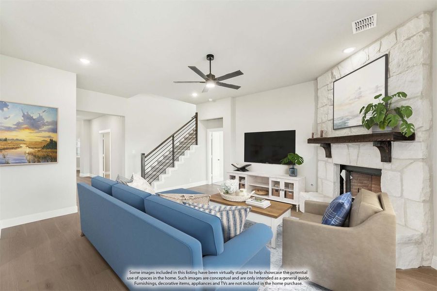 Living room with stone fireplace, ceiling fan, hardwood floors, and staircase with metal railing Living room with stone fireplace, ceiling fan, hardwood floors, and staircase with metal railing