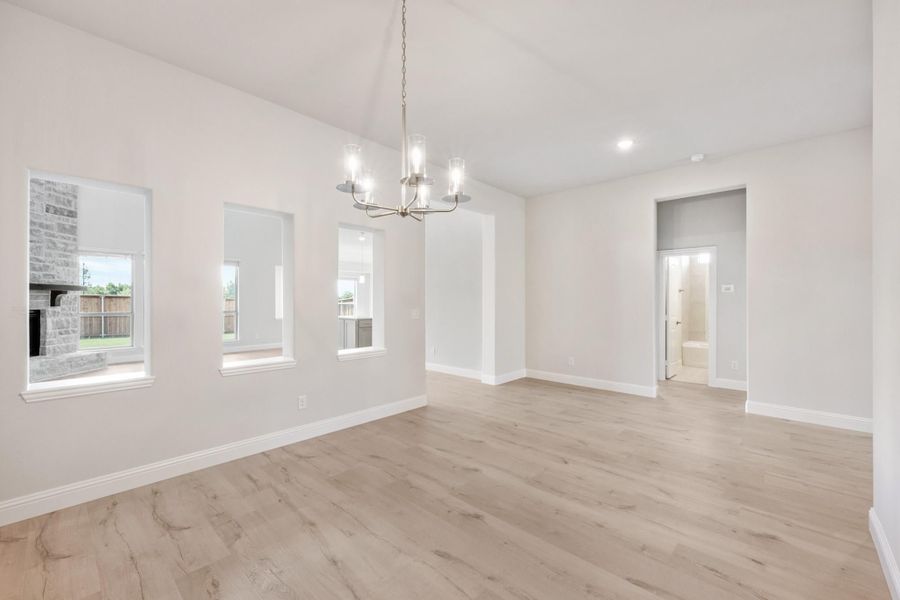 Open dining area with light wood floors, chandelier, and three windows along white walls