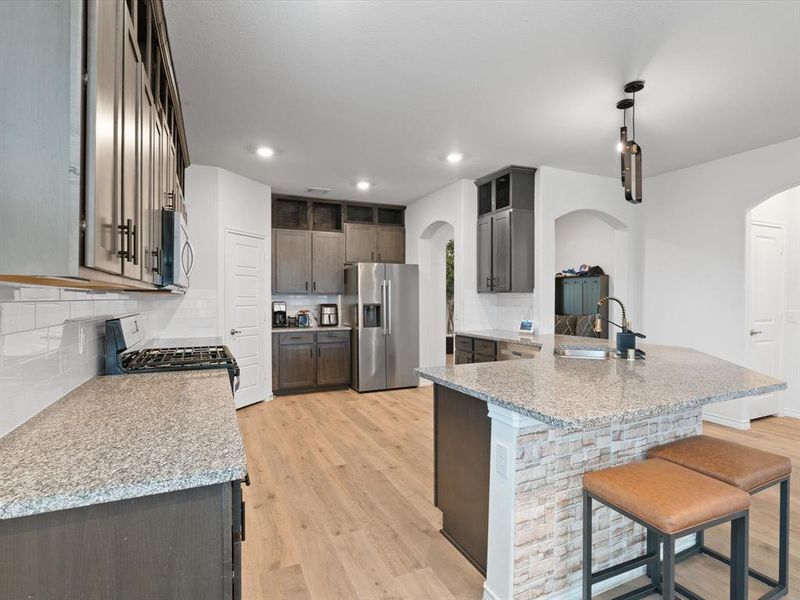 Kitchen featuring appliances with stainless steel finishes, sink, light stone counters, and decorative light fixtures