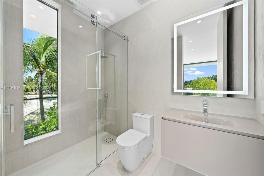 Modern bathroom featuring a glass-enclosed shower with a rainfall showerhead, a floating vanity with an integrated sink, and an illuminated mirror