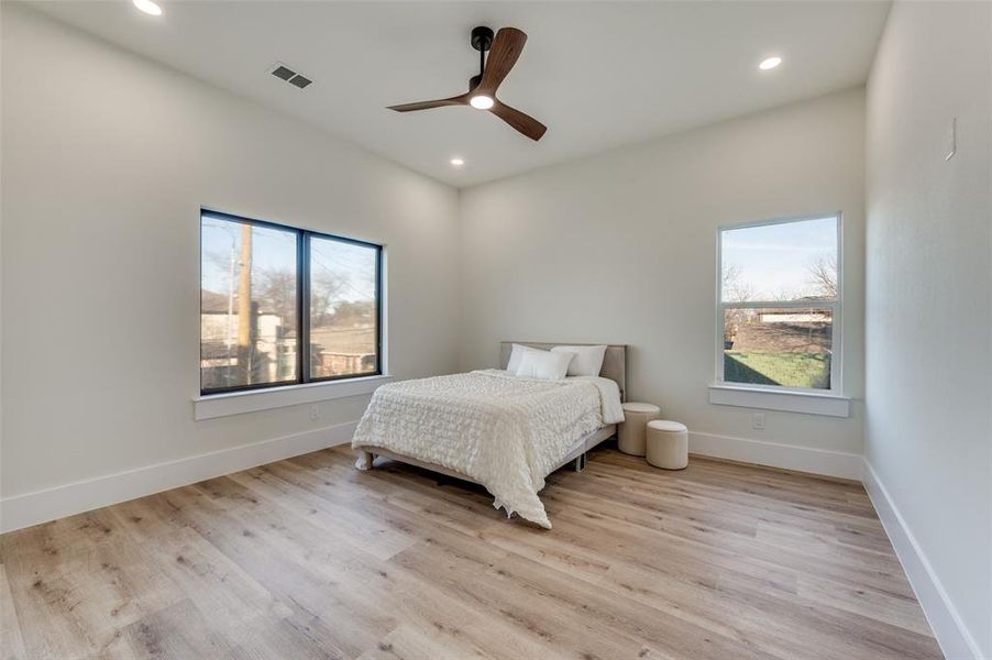 Bright bedroom featuring light wood-finish flooring, recessed lighting, and a modern ceiling fan