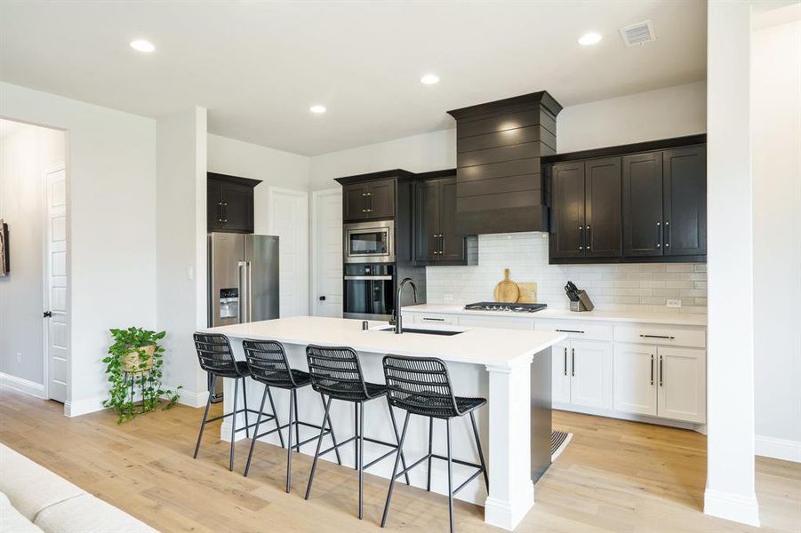 Kitchen with appliances with stainless steel finishes, a sink, a breakfast bar area, light wood-style flooring, and light countertops Kitchen with appliances with stainless steel finishes, a sink, a breakfast bar area, light wood-style flooring, and light countertops