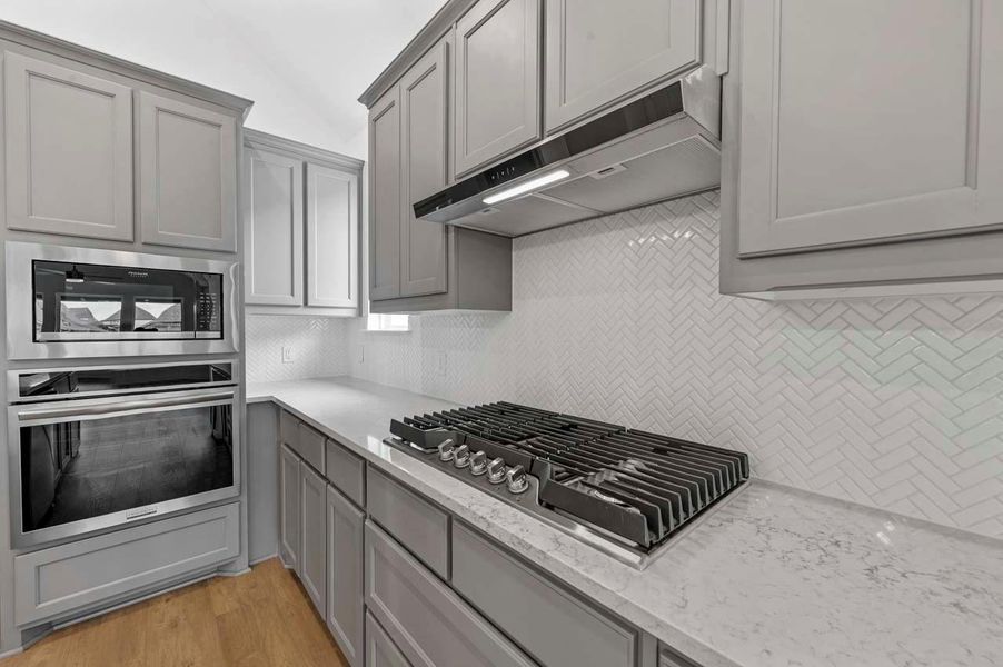 Kitchen with under cabinet range hood, gray cabinetry, appliances with stainless steel finishes, and backsplash