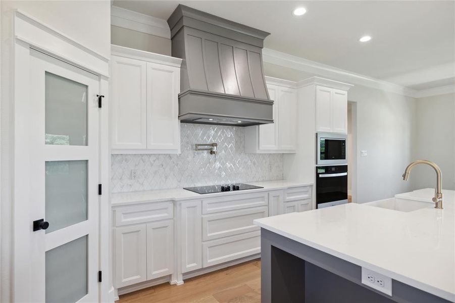 Kitchen featuring black appliances, white cabinets, light wood-type flooring, sink, and custom range hood