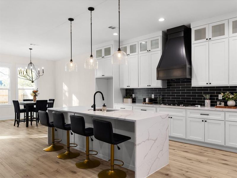 Modern kitchen featuring a waterfall-edge island with seating, white shaker-style cabinetry, a black subway tile backsplash, a dark wood range hood, and wood-finish flooring