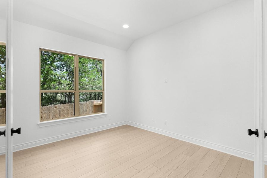 A well-lit bedroom features hardwood flooring, offering views of the natural outdoor surroundings through a large window.