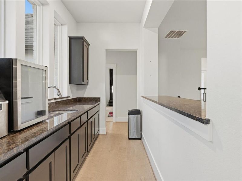 Wet bar featuring dark wood-finish cabinetry, a single basin sink with a gooseneck faucet, and light wood-finish flooring Wet bar featuring dark wood-finish cabinetry, a single basin sink with a gooseneck faucet, and light wood-finish flooring