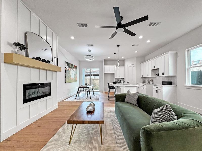 Living area with a large fireplace, healthy amount of natural light, a ceiling fan, recessed lighting, and light wood-type flooring