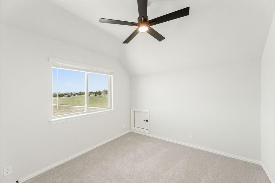 Empty bedroom with vaulted ceiling, ceiling fan, carpet flooring, and window with outdoor views