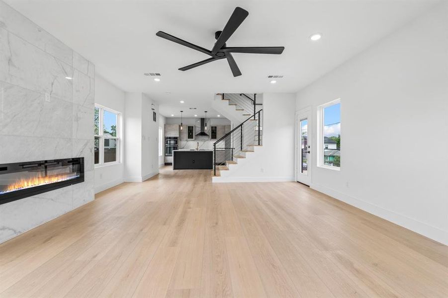 Unfurnished living room featuring stairs, light wood-style floors, a tiled fireplace, visible vents, and recessed lighting