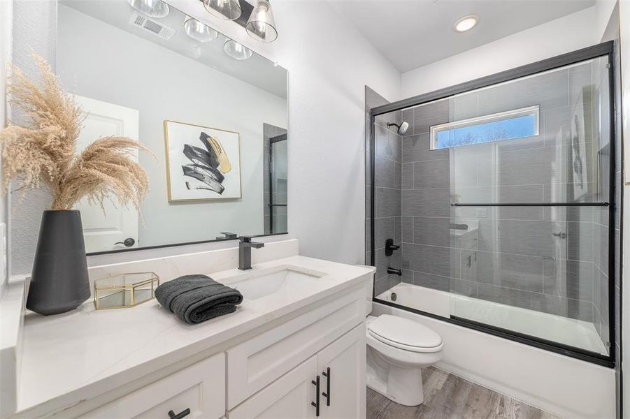 Full bathroom with wood-type flooring, combined bath / shower with glass door, vanity, and toilet