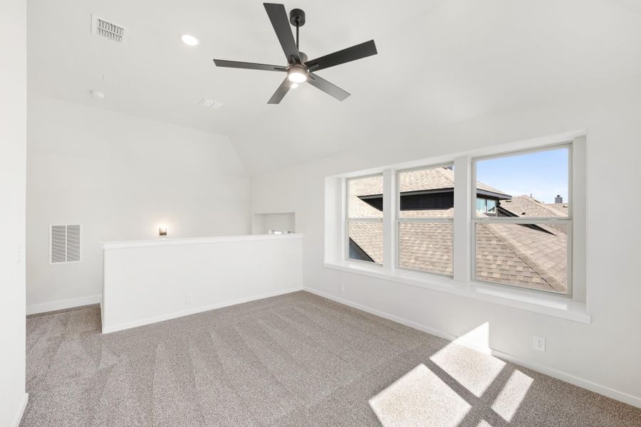Empty bedroom with vaulted ceiling, ceiling fan, carpet flooring, and large windows overlooking rooftops