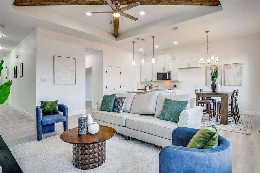 Living room with light wood-type flooring, recessed lighting, a ceiling fan, a chandelier, and a raised ceiling Living room with light wood-type flooring, recessed lighting, a ceiling fan, a chandelier, and a raised ceiling