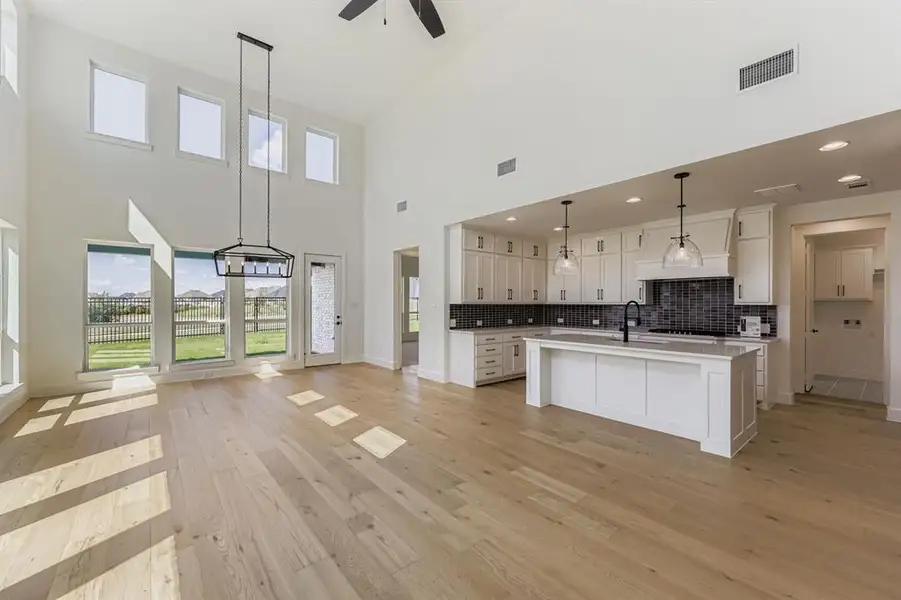 Kitchen with open floor plan, tasteful backsplash, a center island with sink, light wood-style floors, and hanging light fixtures