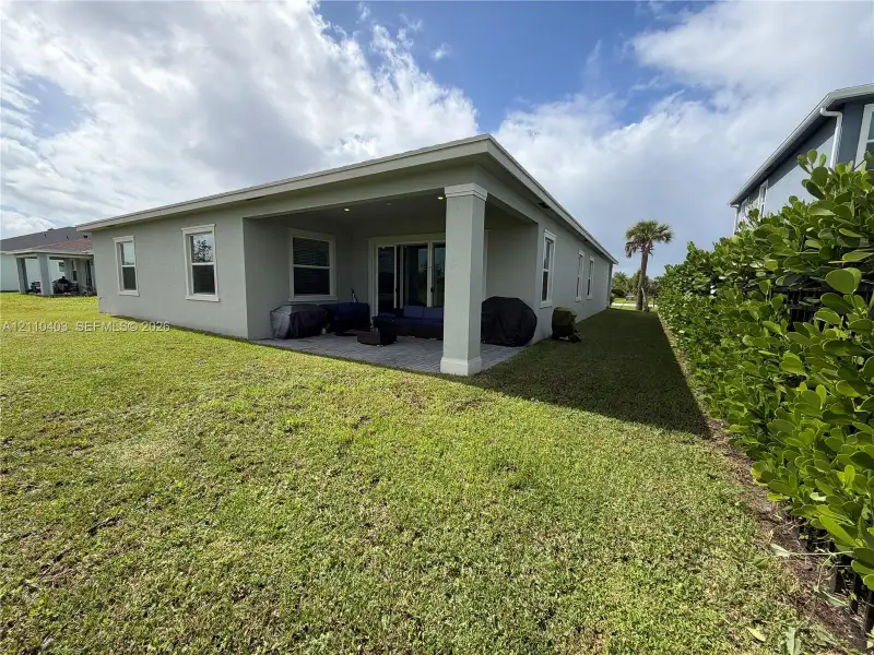 Covered concrete patio featuring recessed lighting and stucco exterior finish, surrounded by a spacious lawn and perimeter shrubbery