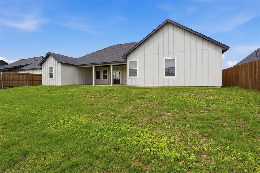 Expansive backyard featuring a lush green lawn, full privacy fencing, and a covered patio area with a sliding glass door