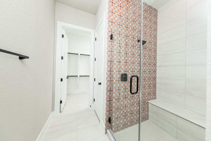 The walk-in shower includes a convenient, integrated white bench, offering comfort and a high-end, custom appearance. This modern shower features a striking two-tile design that balances bold patterns with clean, neutral surfaces.