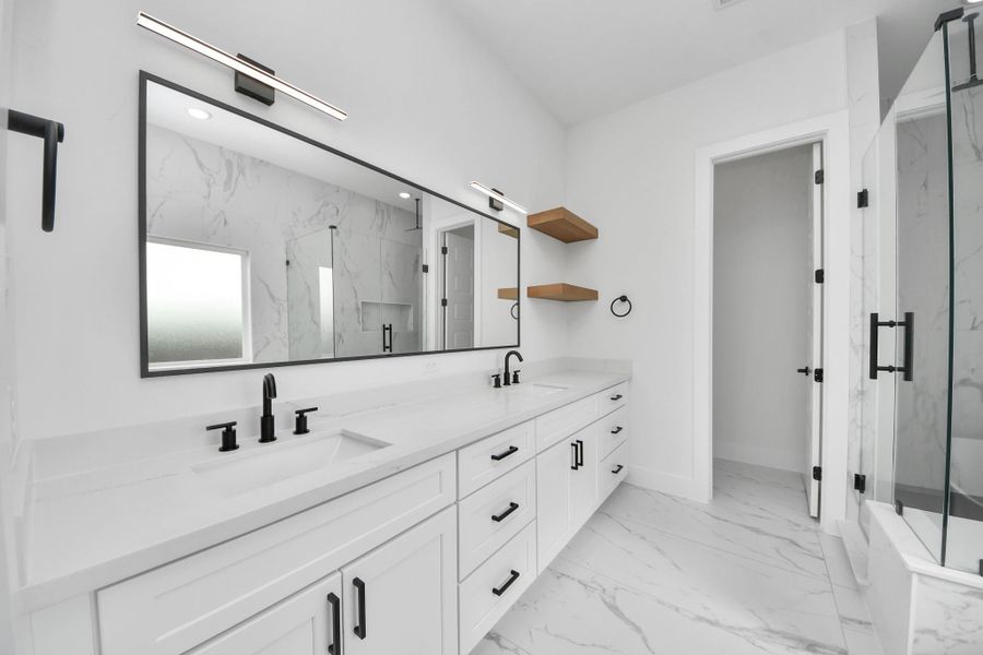 This bathroom features a sleek, modern design with white cabinetry, dual sinks, and black fixtures. It includes a large mirror, a spacious glass-enclosed shower, and elegant marble-patterned tiles for a luxurious feel.