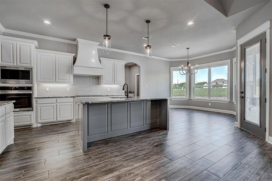 Kitchen featuring white cabinets, custom exhaust hood, stainless steel appliances, and a kitchen island with sink