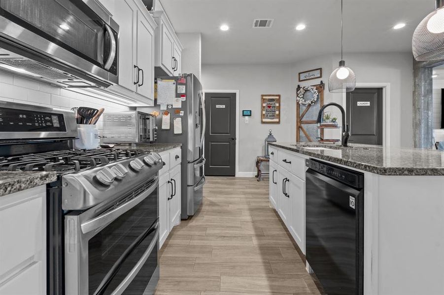 Kitchen featuring appliances with stainless steel finishes, white cabinetry, pendant lighting, and dark stone countertops