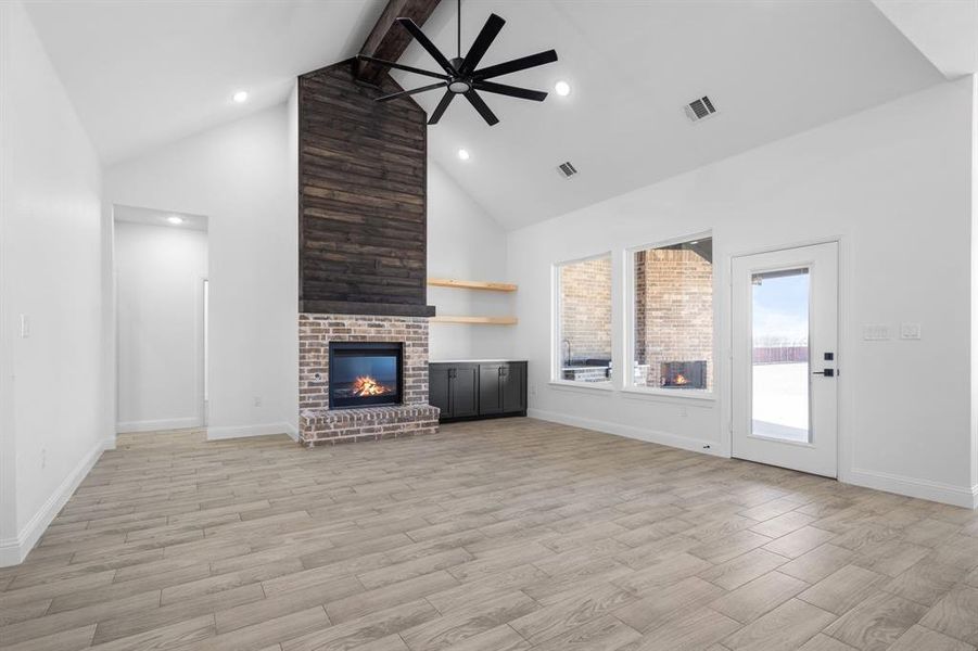 Unfurnished living room featuring light hardwood / wood-style flooring, ceiling fan, high vaulted ceiling, a brick fireplace, and beamed ceiling