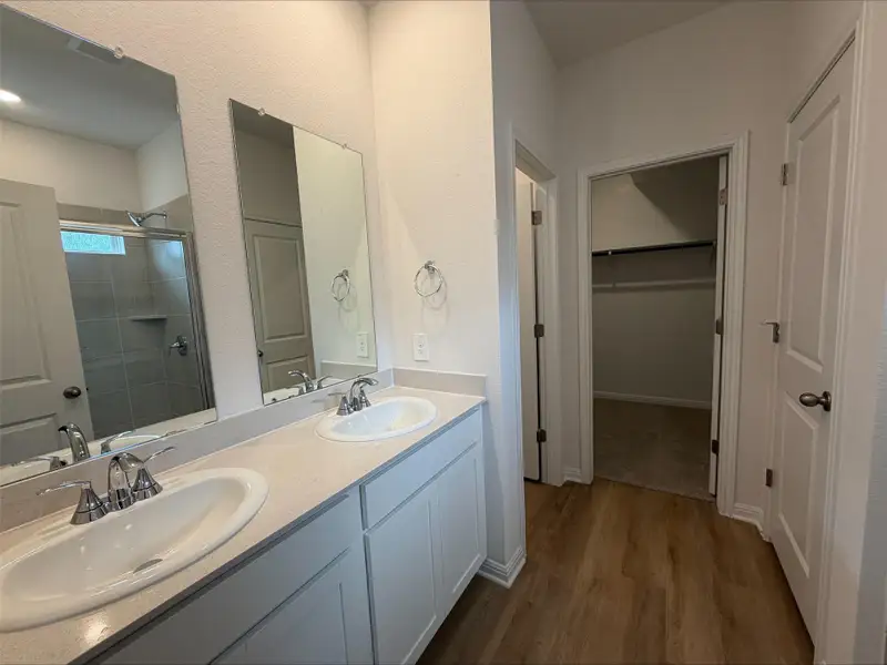 Bathroom featuring dark wood finished floors, a stall shower, double vanity, and a walk in closet