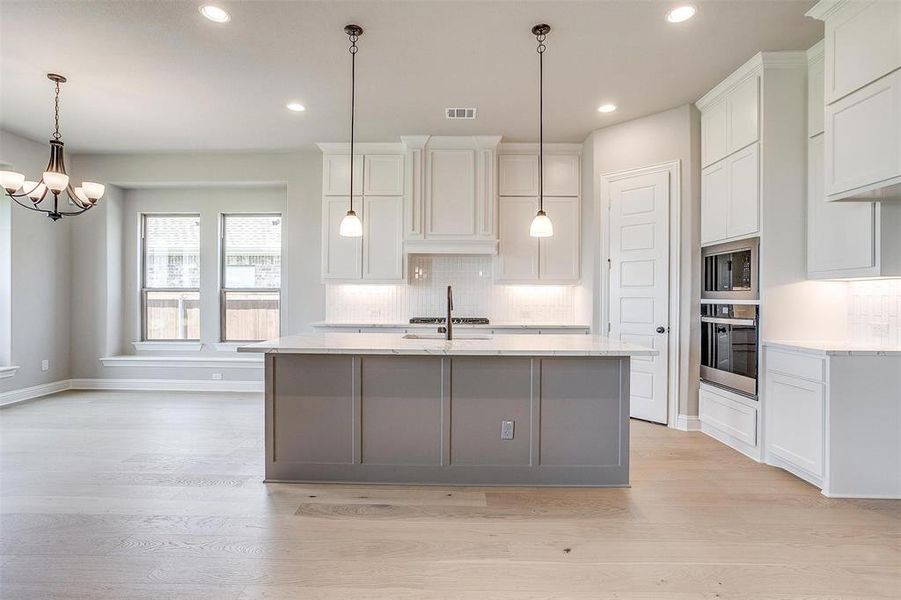 Kitchen featuring an island with sink, tasteful backsplash, oven, white cabinetry, and light wood-type flooring