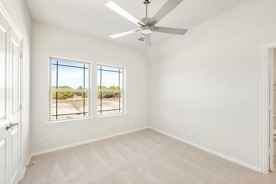 Empty bedroom with ceiling fan, carpet flooring, and two windows with desert views Empty bedroom with ceiling fan, carpet flooring, and two windows with desert views